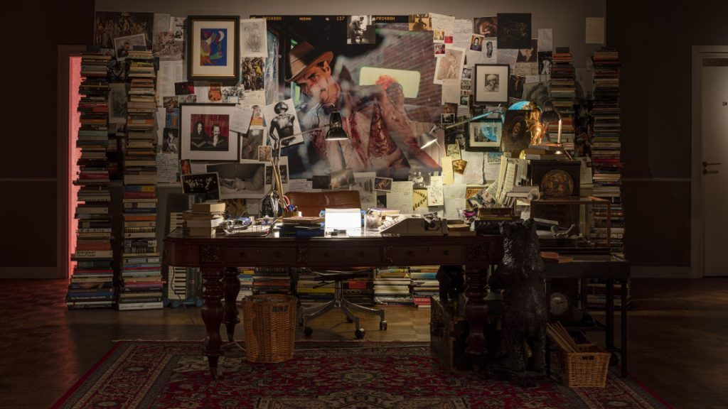 Installation view of Nick Cave's "Stranger Than Kindness" exhibition, showing a writing desk, typewriter and densely papered wall.